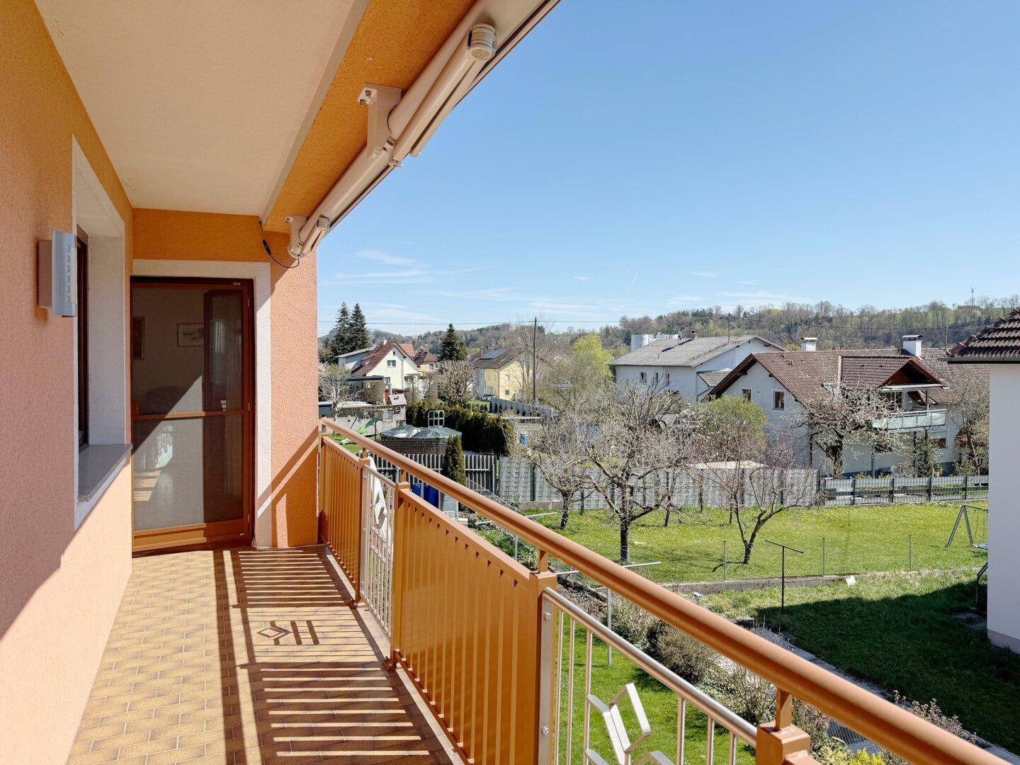 Sonniger Balkon mit Fliesenboden und weitem Blick über die grüne Umgebung.