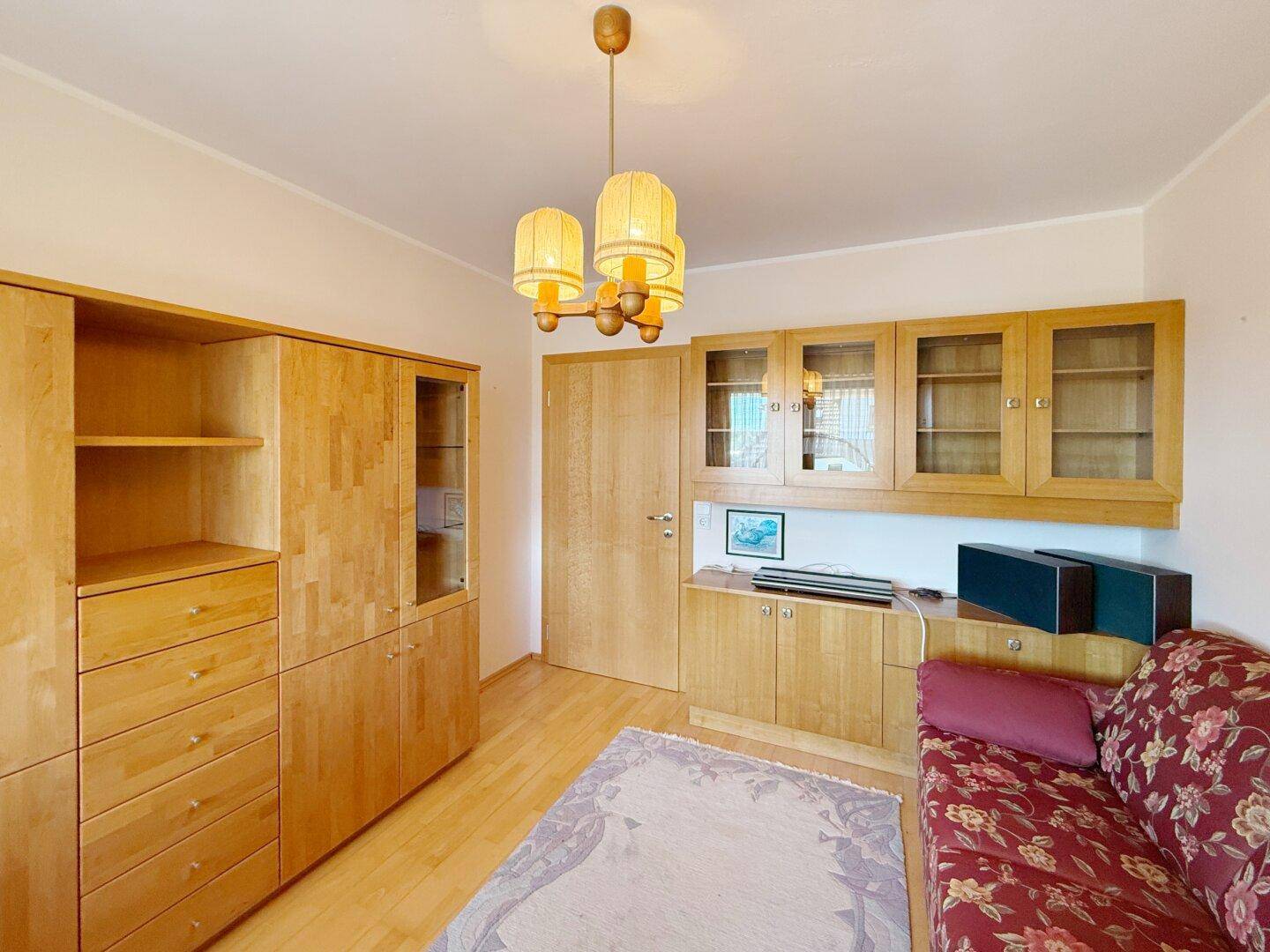 Helles Zimmer mit Holzmöbeln, Parkettboden und gemütlicher Sitzgelegenheit.