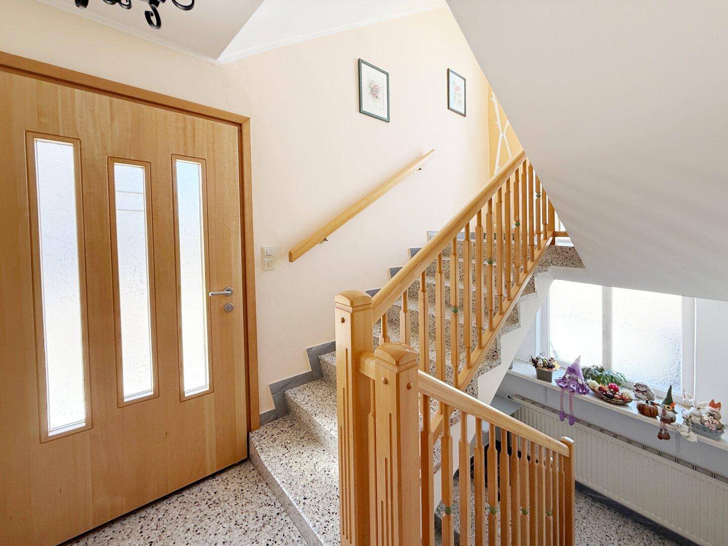Heller Flur mit Holztreppe und Terrazzoboden, der die Etagen verbindet.