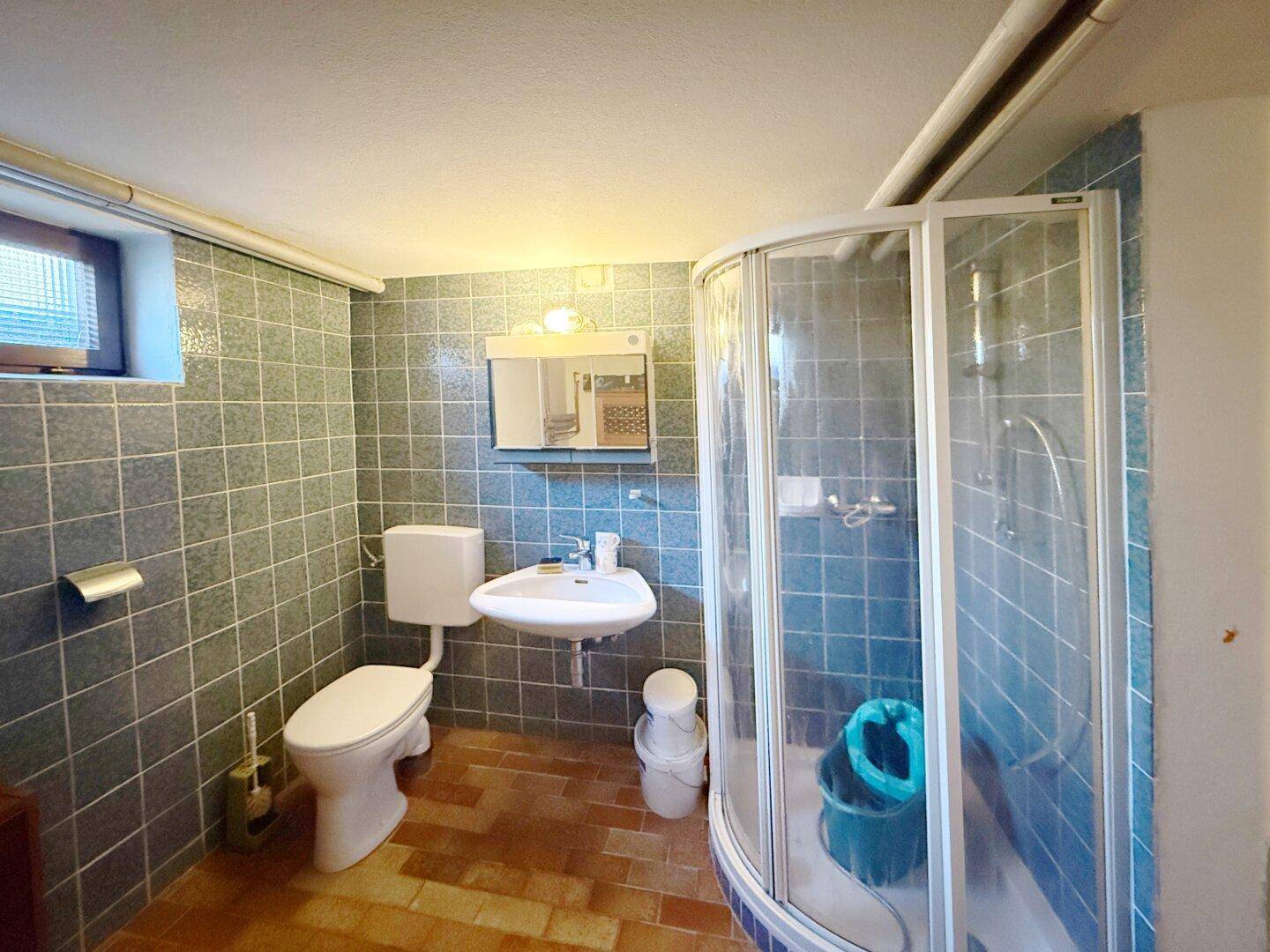 Gefliestes Badezimmer im Keller mit Dusche, WC und Waschbecken.