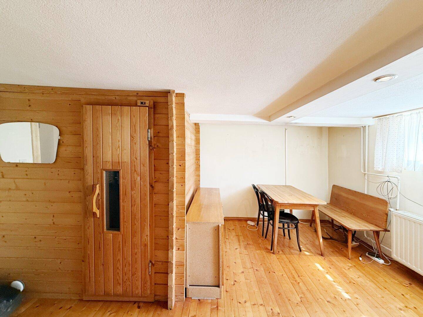 Gemütlicher Kellerraum mit Sauna, Holzboden und Sitzgelegenheiten.