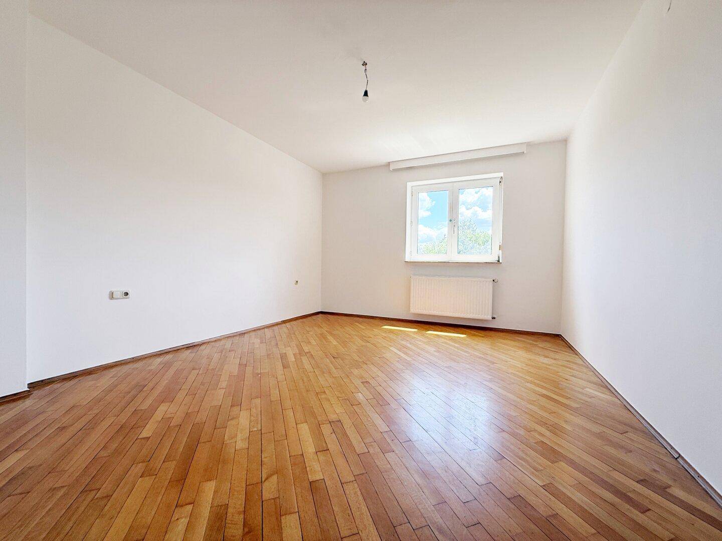 Geräumiger Wohnbereich mit klassischem Parkettboden und großem Fenster für viel Licht.