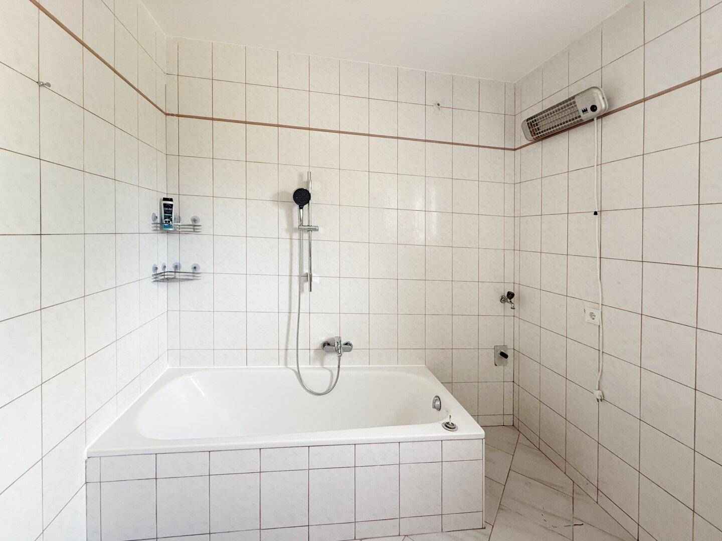 Helles Badezimmer mit Badewanne, weißen Fliesen und Heizkörper an der Wand.