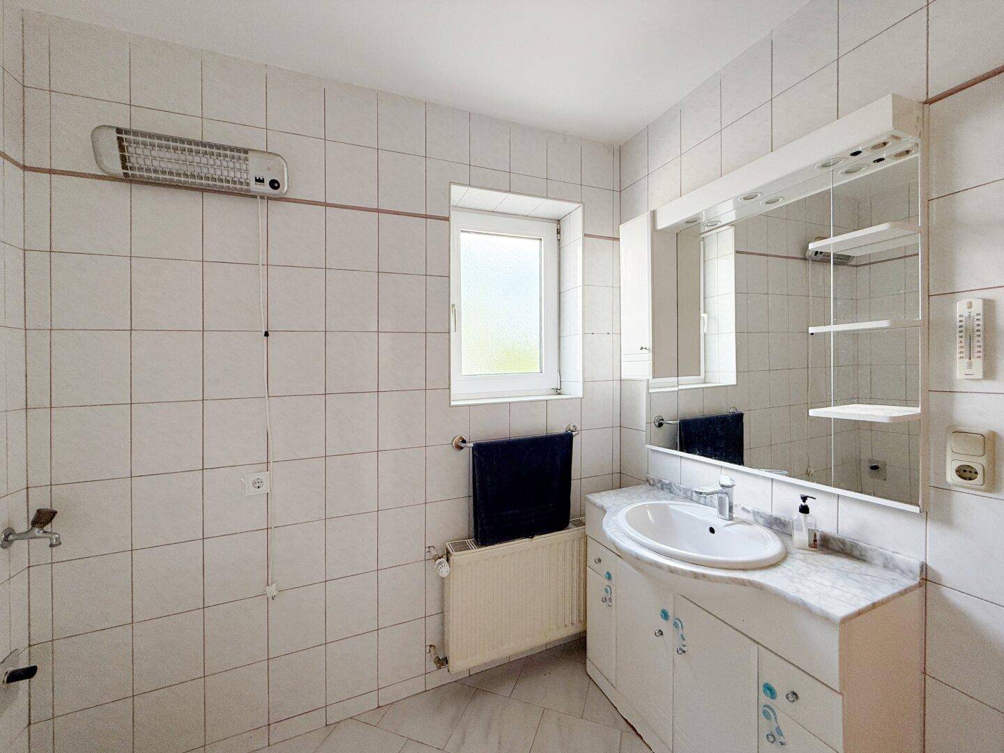 Gefliestes Badezimmer mit Waschtisch, Spiegelschrank und Fenster für Tageslicht.