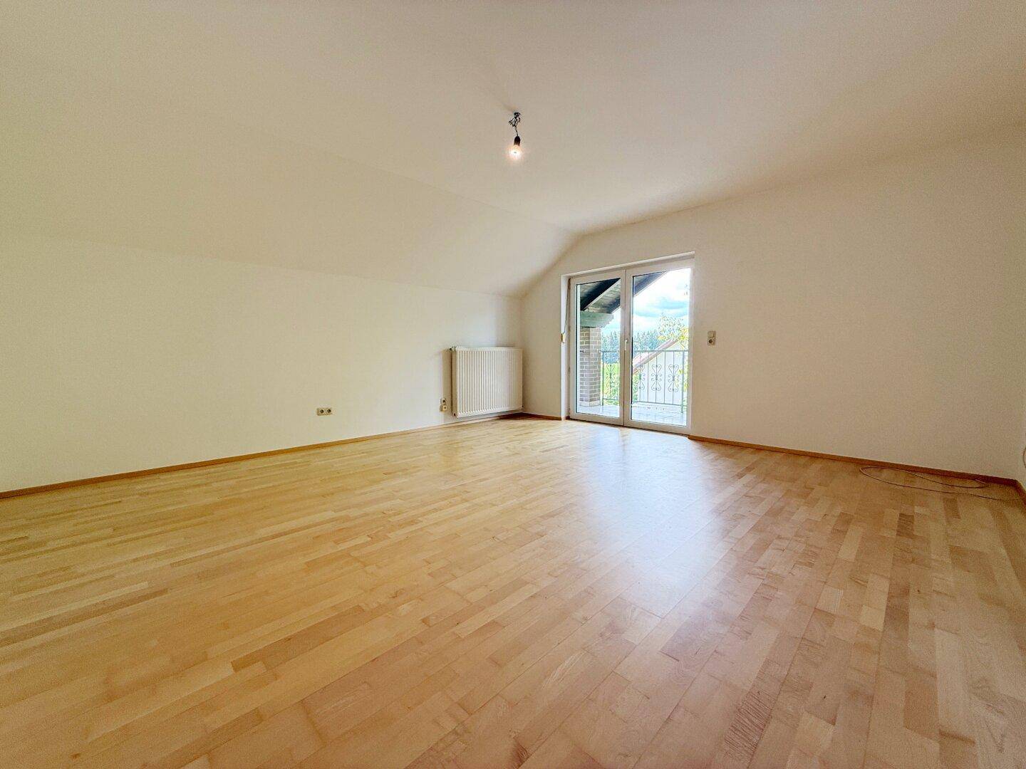Geräumiges Schlafzimmer mit hellem Parkettboden und Zugang zu einem französischen Balkon.