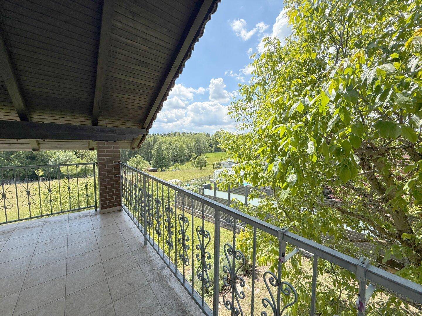 Überdachter Balkon mit weitem Blick über die grüne Landschaft und Wälder.