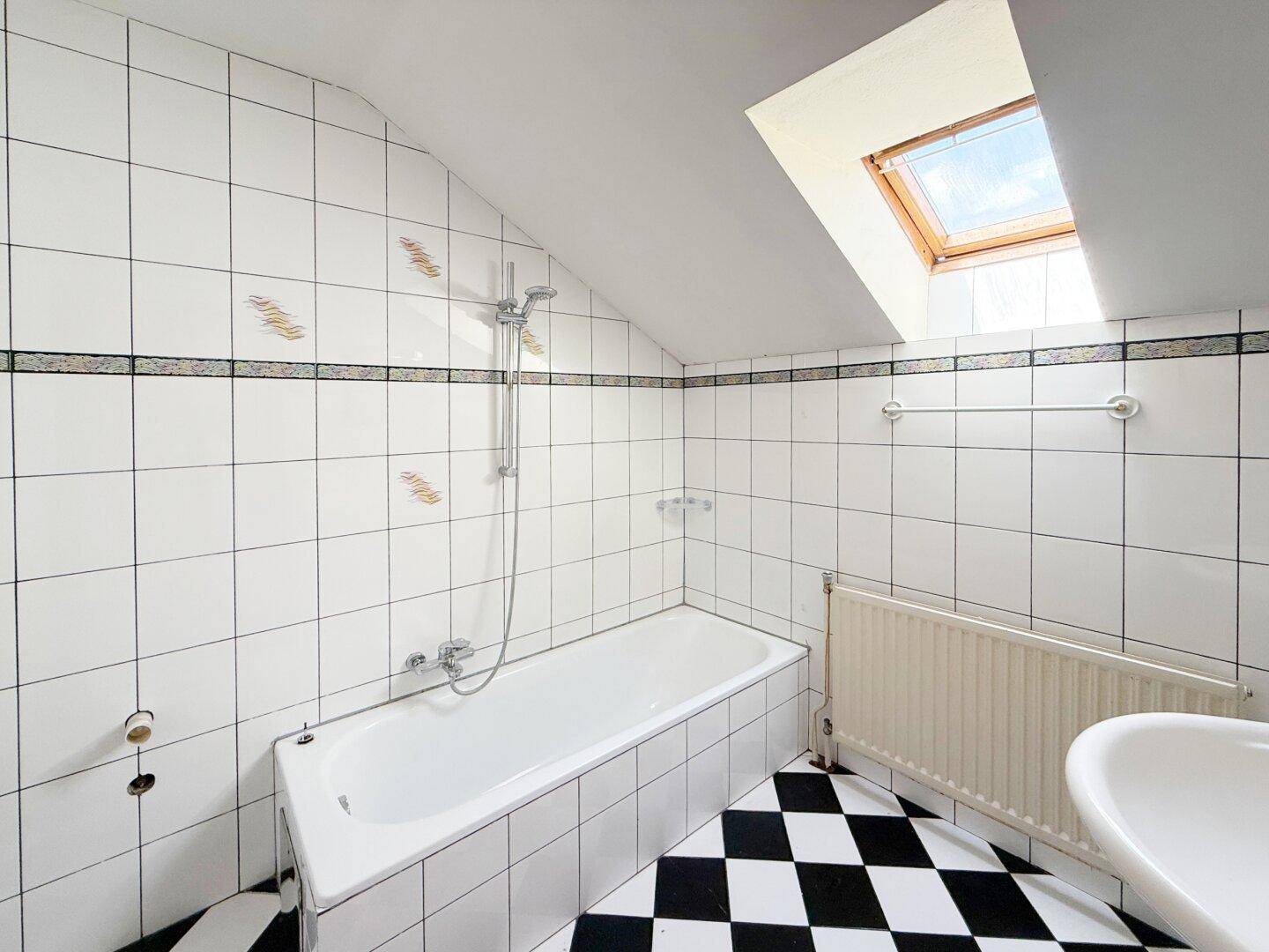 Helles Badezimmer mit Badewanne, weißen Fliesen und Dachfenster im Dachgeschoss.