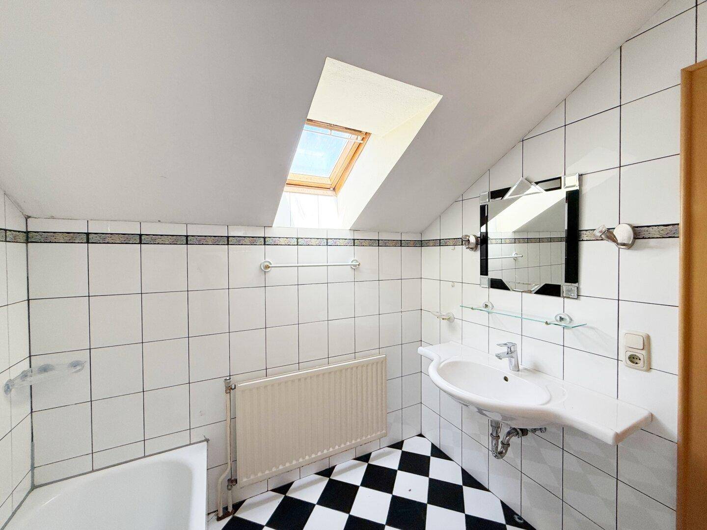 Badezimmer im Dachgeschoss mit Schachbrettmuster-Fliesen und Dachfenster für Helligkeit.