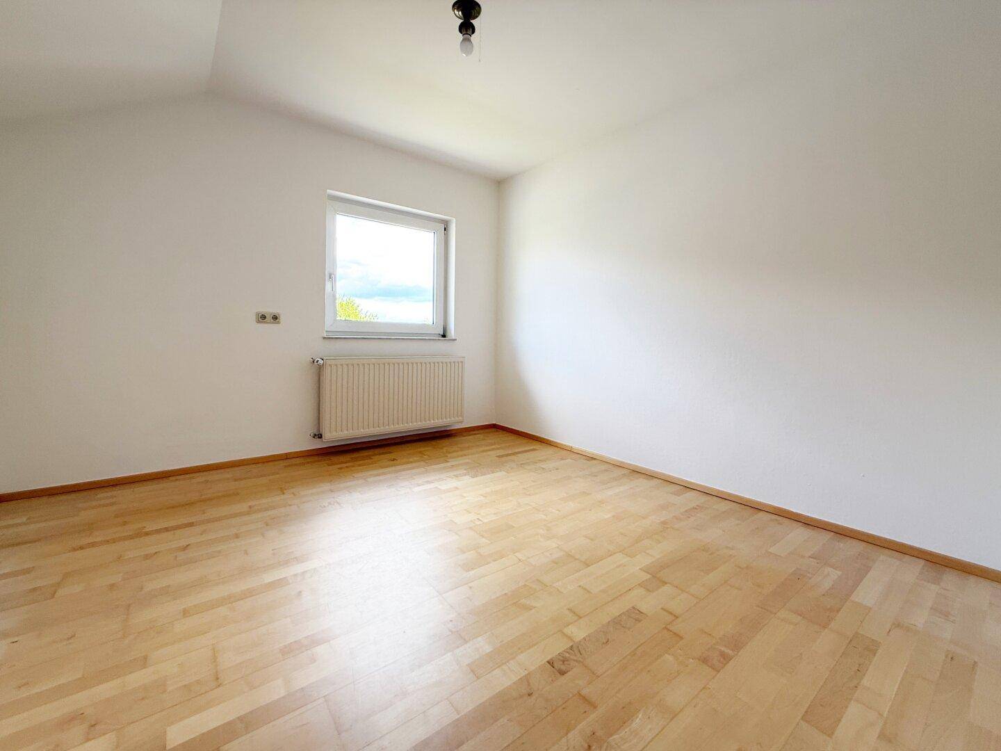 Helles Schlafzimmer mit Holzboden, Dachschräge und Fenster mit Blick ins Grüne.