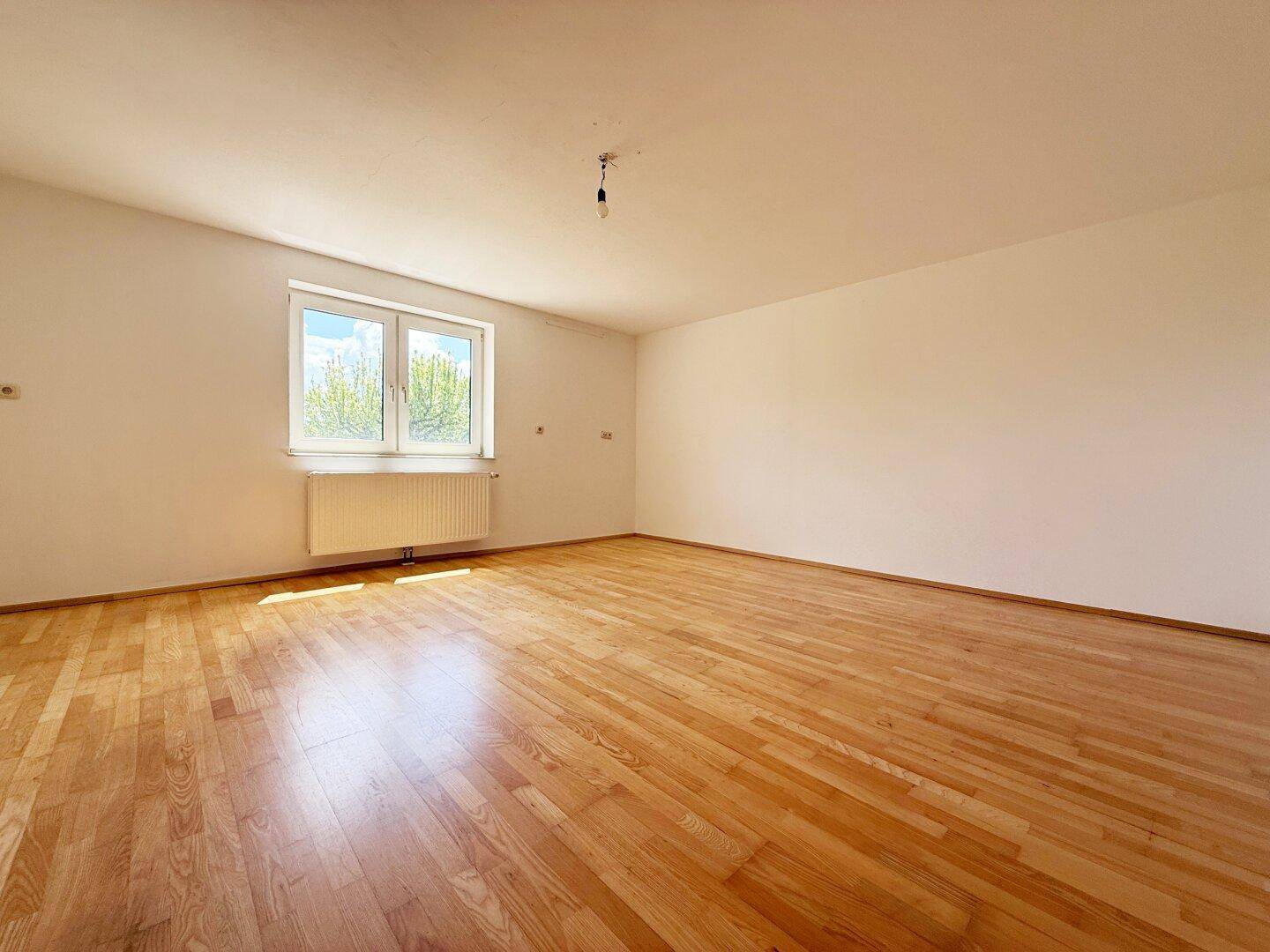 Heller Wohnraum mit Parkettboden und großem Fenster, das viel Tageslicht hereinlässt.