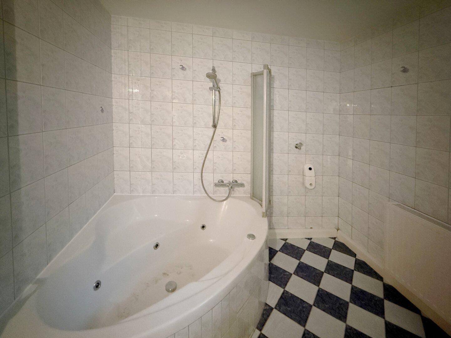 Badezimmer mit Eckbadewanne, Duschbereich und schwarz-weiß karierten Bodenfliesen.