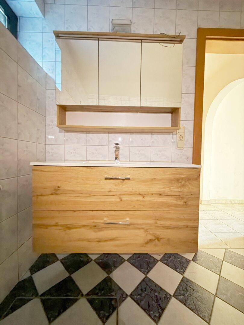 Badezimmer mit modernem Holzwaschtisch, Einzelwaschbecken und Spiegelschrank.