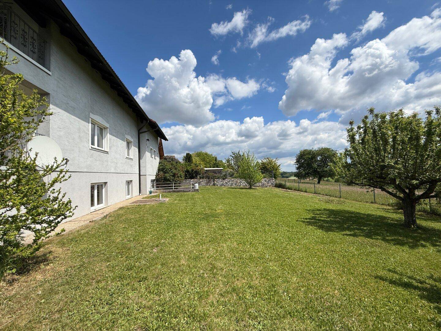 Seitenansicht des Hauses mit weißer Fassade, Fenstern und weitläufigem Gartenbereich.