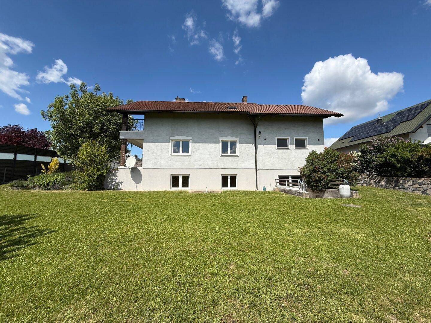 Rückansicht des Hauses mit weitläufigem Rasen und sonnigem Gartenbereich.