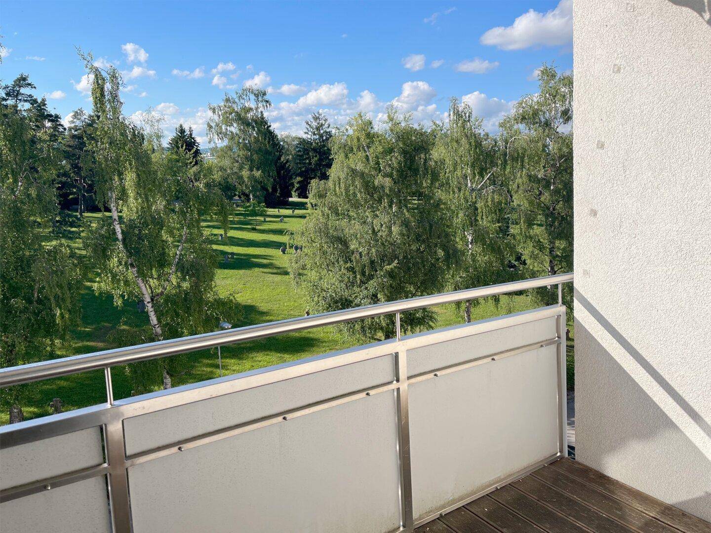 Balkon mit Holzboden und weitem Blick ins Grüne mit vielen Bäumen.