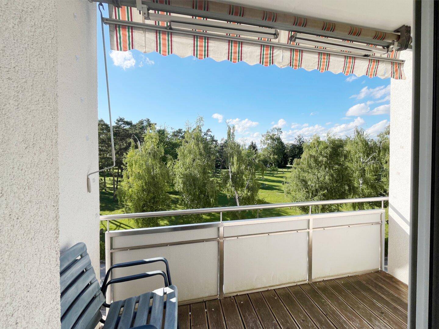 Sonniger Balkon mit Markise, Holzboden und freiem Blick auf die grüne Umgebung.