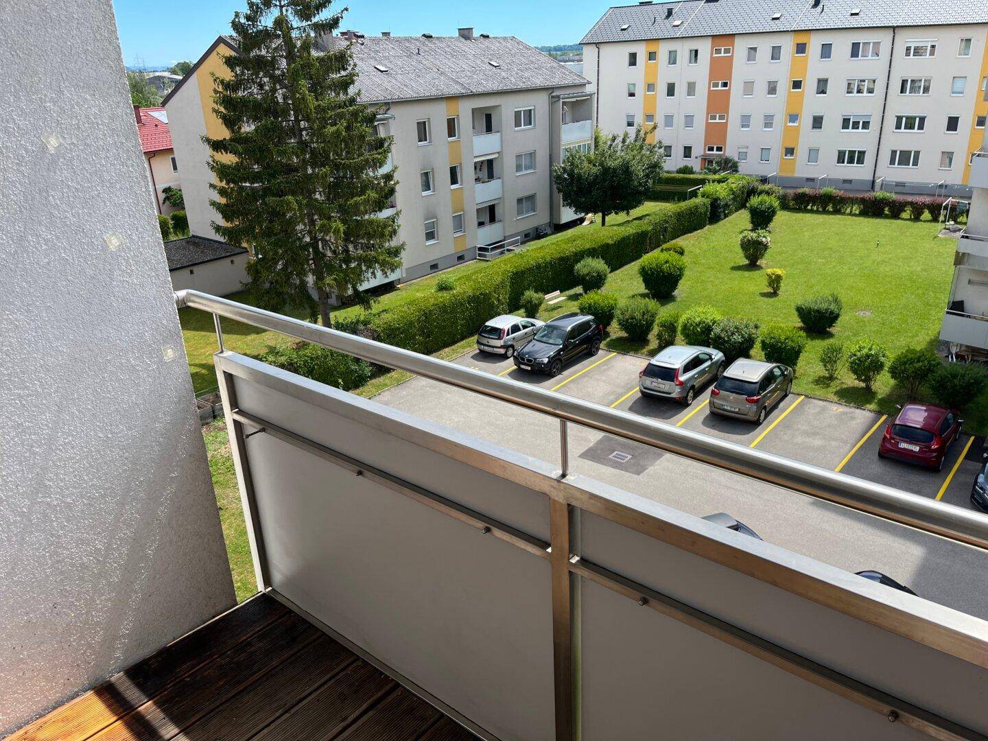 Balkon mit Holzboden und Aussicht auf den Parkplatz und gepflegte Grünflächen.