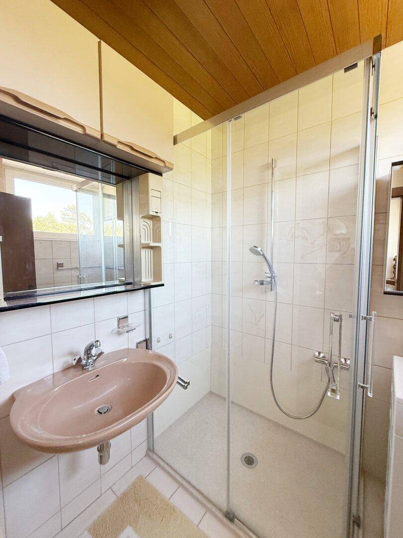 Badezimmer mit Duschkabine, Waschbecken und hellen Fliesen an Wänden und Boden.