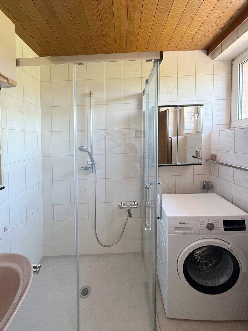 Badezimmer mit Duschkabine, Waschmaschine und Fenster für natürliches Licht.