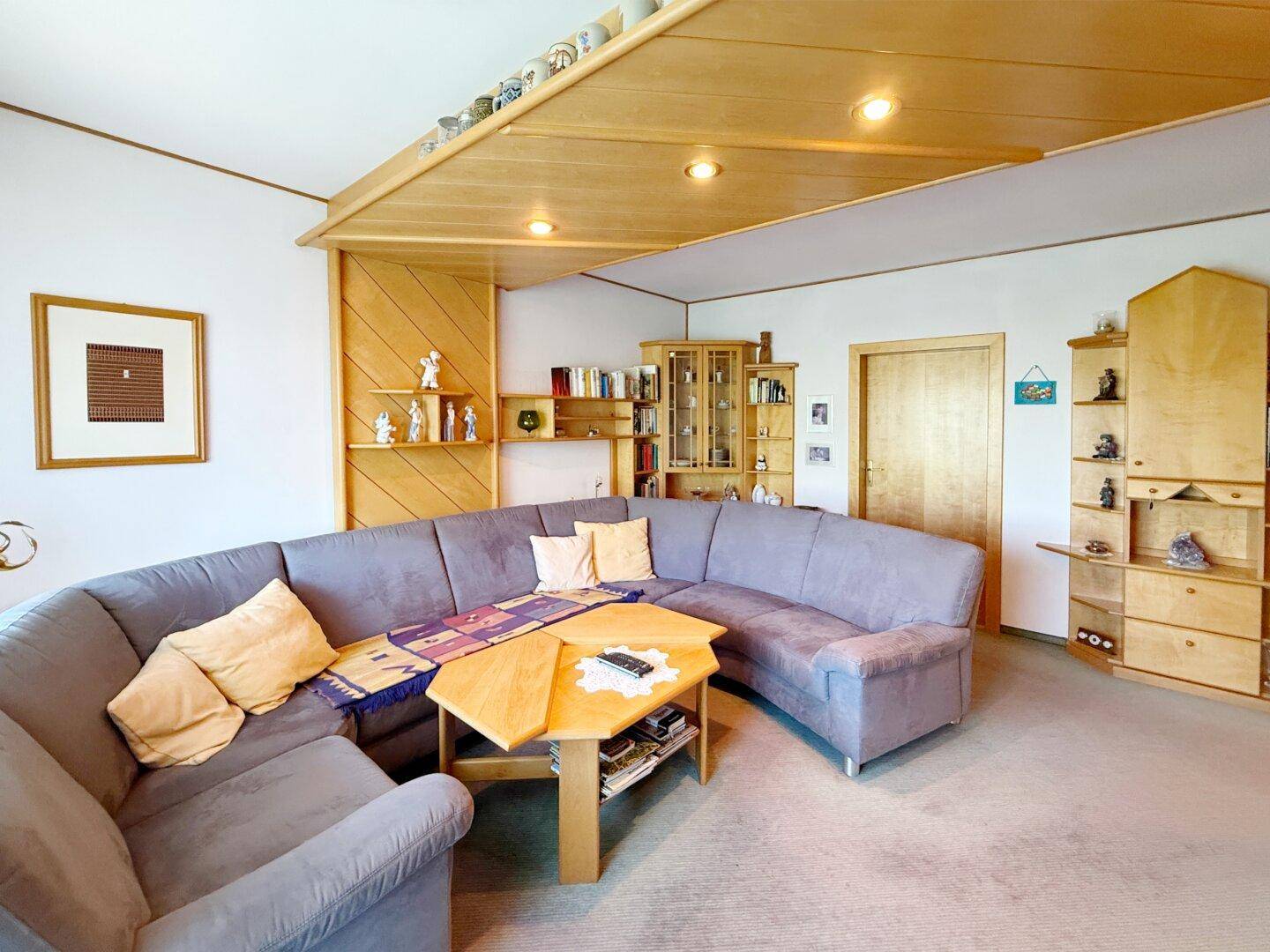 Gemütliches Wohnzimmer mit großer Eckcouch, Holzdecke und integrierten Holzregalen.
