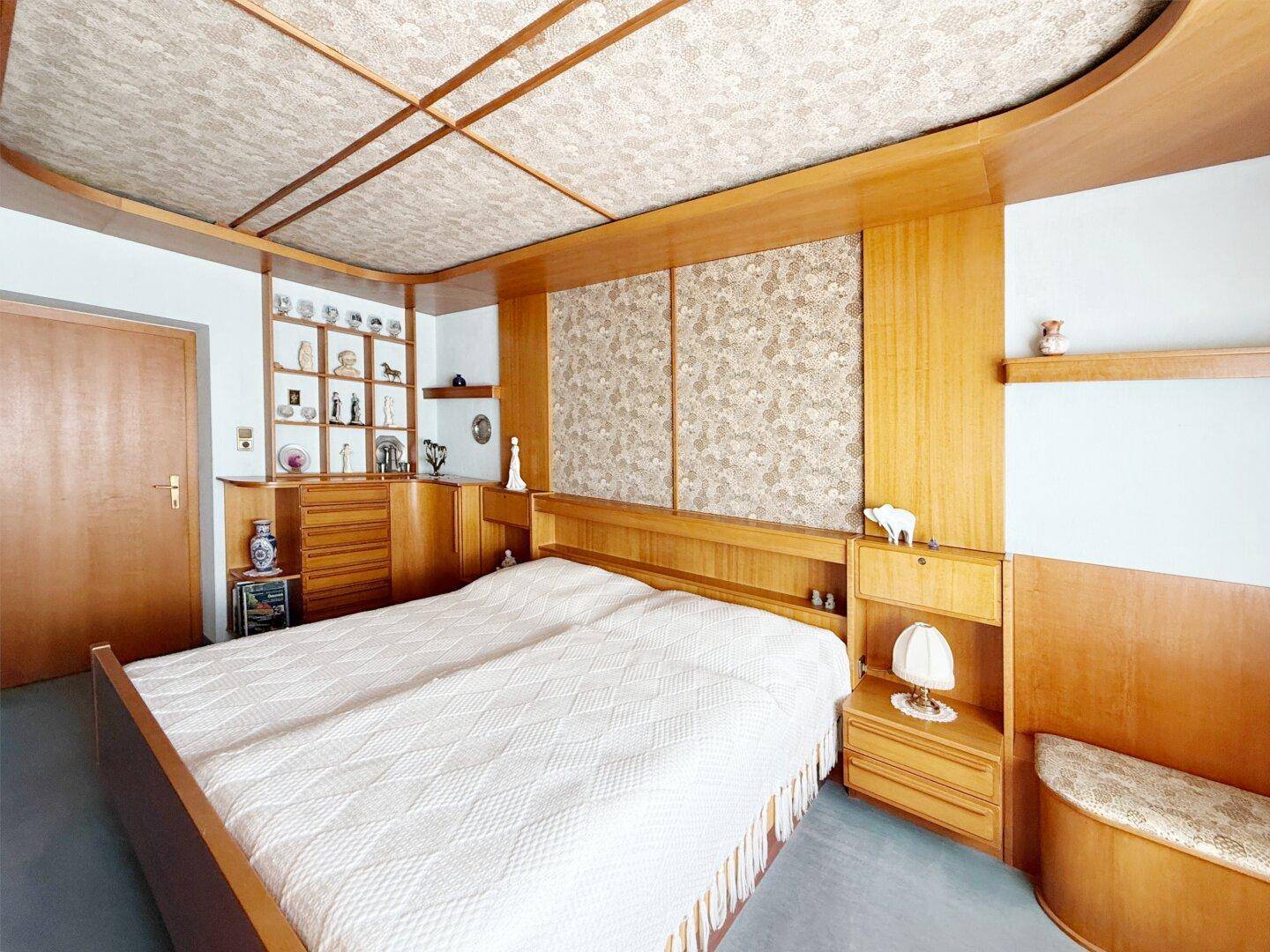 Schlafzimmer mit Holzmöbeln, integrierten Regalen und einem großen Doppelbett.