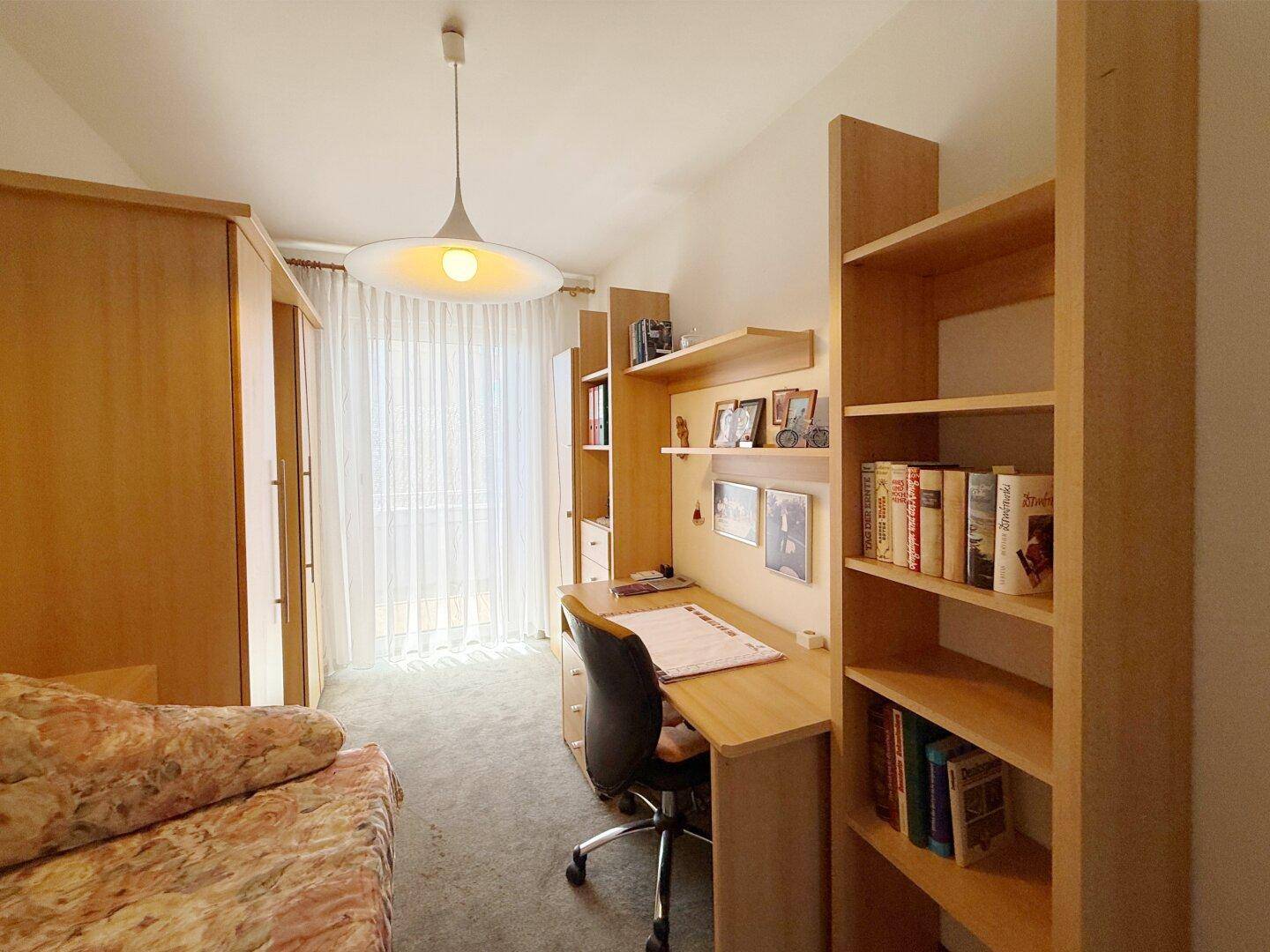 Arbeitszimmer mit Schreibtisch, Bücherregalen und Tageslicht durch große Fenster.