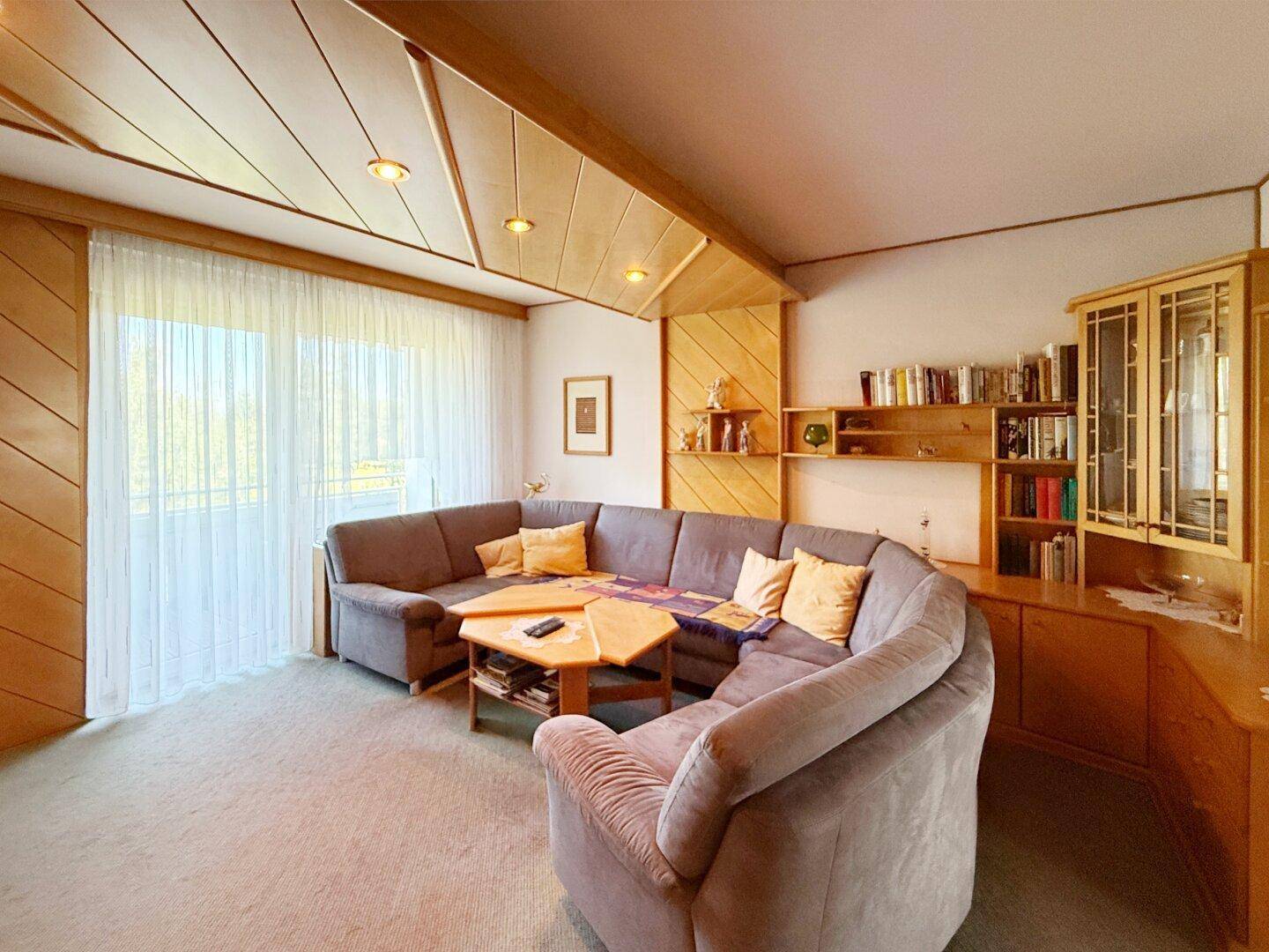 Helles Wohnzimmer mit bequemer Eckcouch, Holzdecke und großen Fenstern mit Vorhängen.