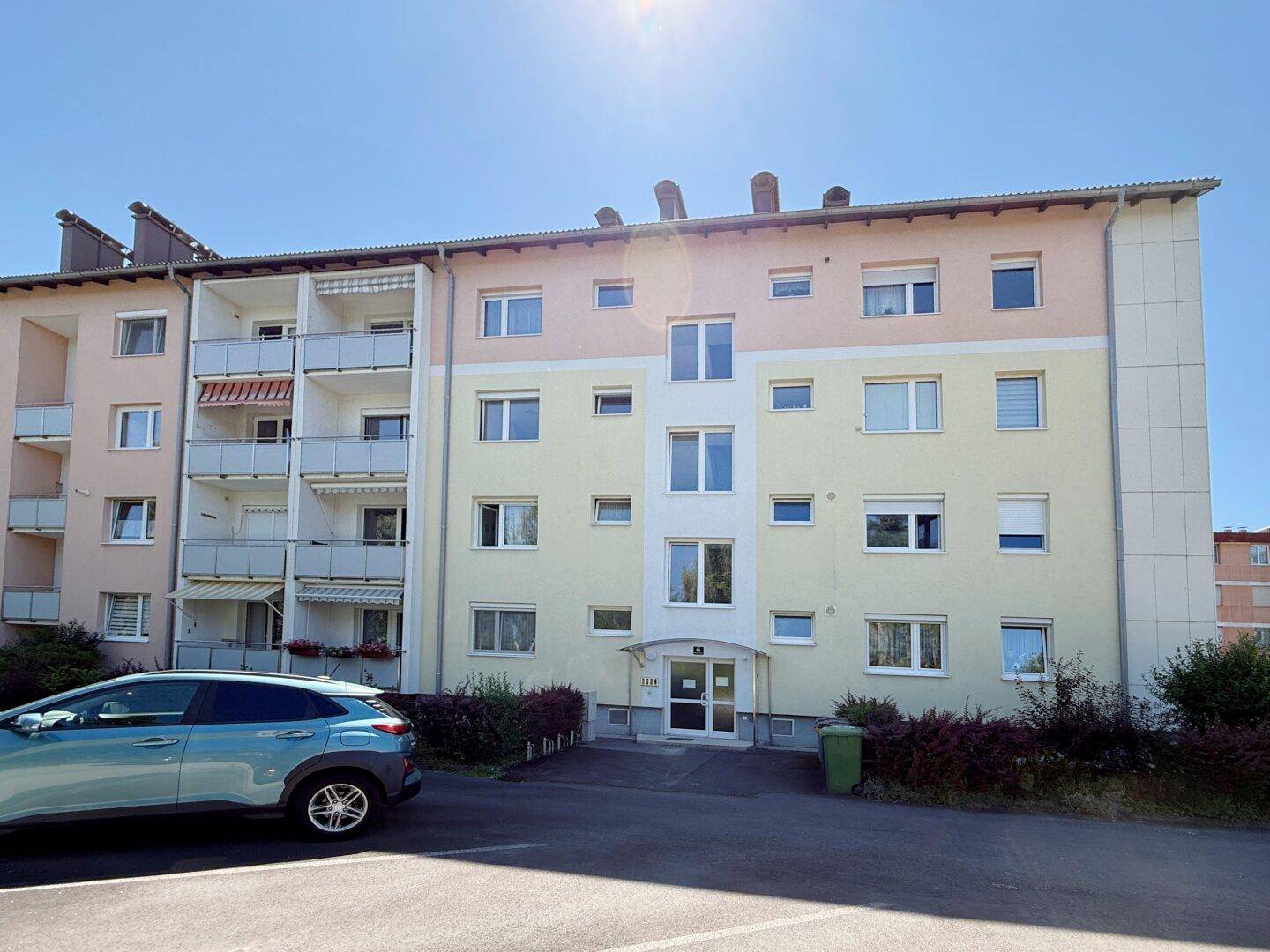 Vorderansicht eines Mehrfamilienhauses mit Eingangsbereich und Parkplätzen.