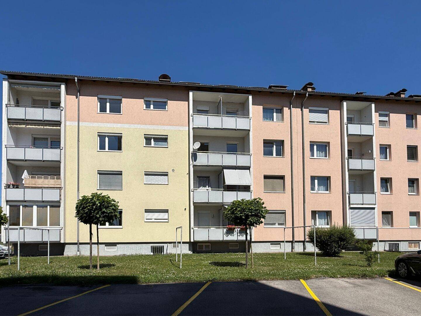 Seitenansicht des Mehrfamilienhauses mit Balkonen, Grünflächen und Parkplätzen.
