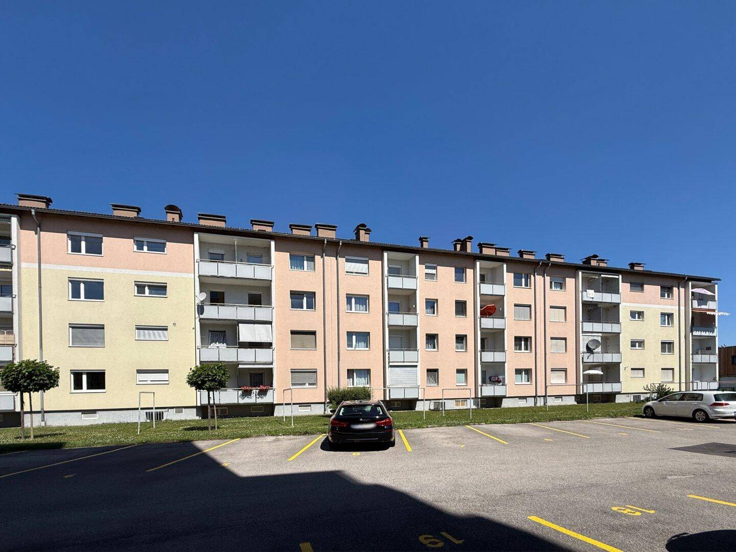 Gesamtansicht des Mehrfamilienhauses mit farbiger Fassade und vielen Parkplätzen.
