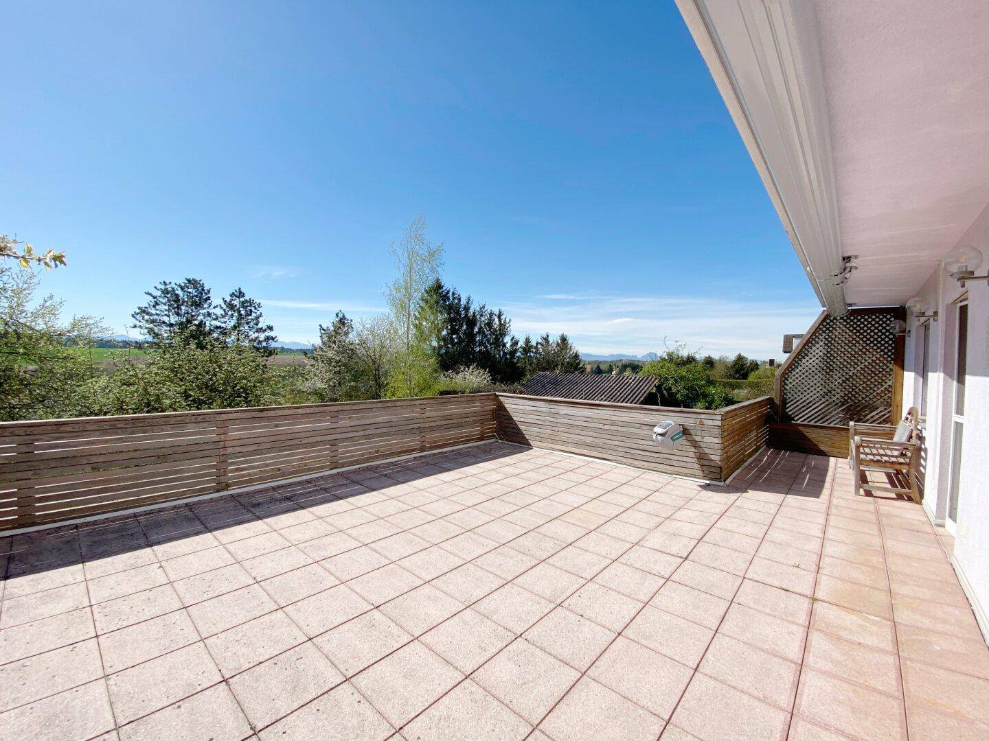 Große geflieste Terrasse mit Holzgeländer und weitem Blick über die grüne Landschaft.