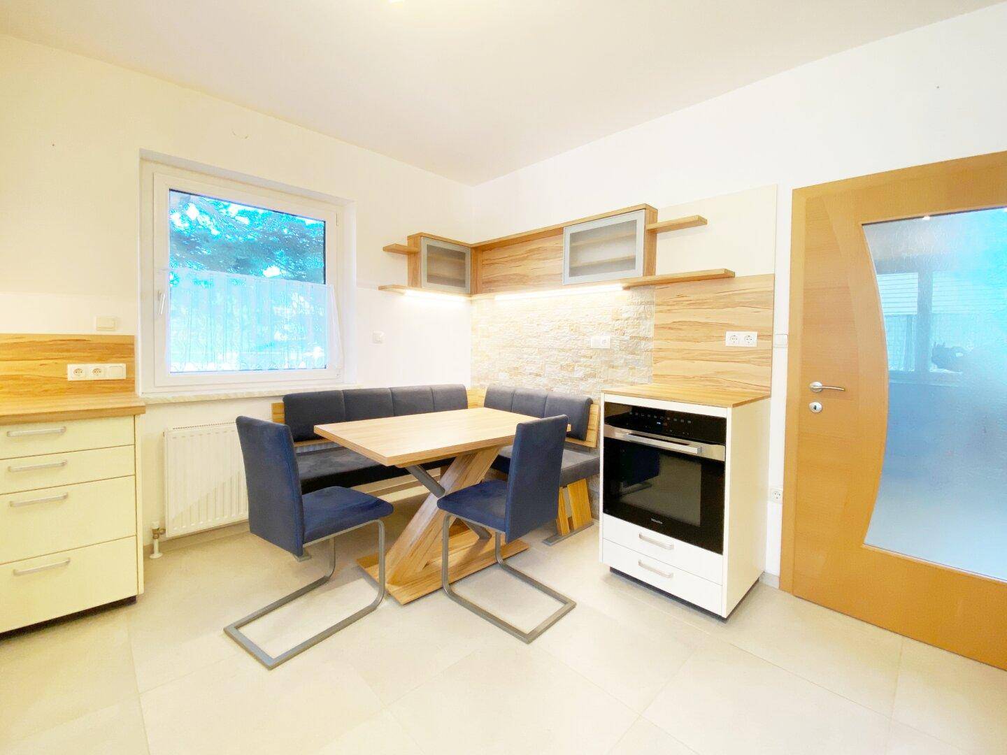 Gemütlicher Essbereich in der Küche mit Holztisch, Sitzbank und integriertem Backofen.
