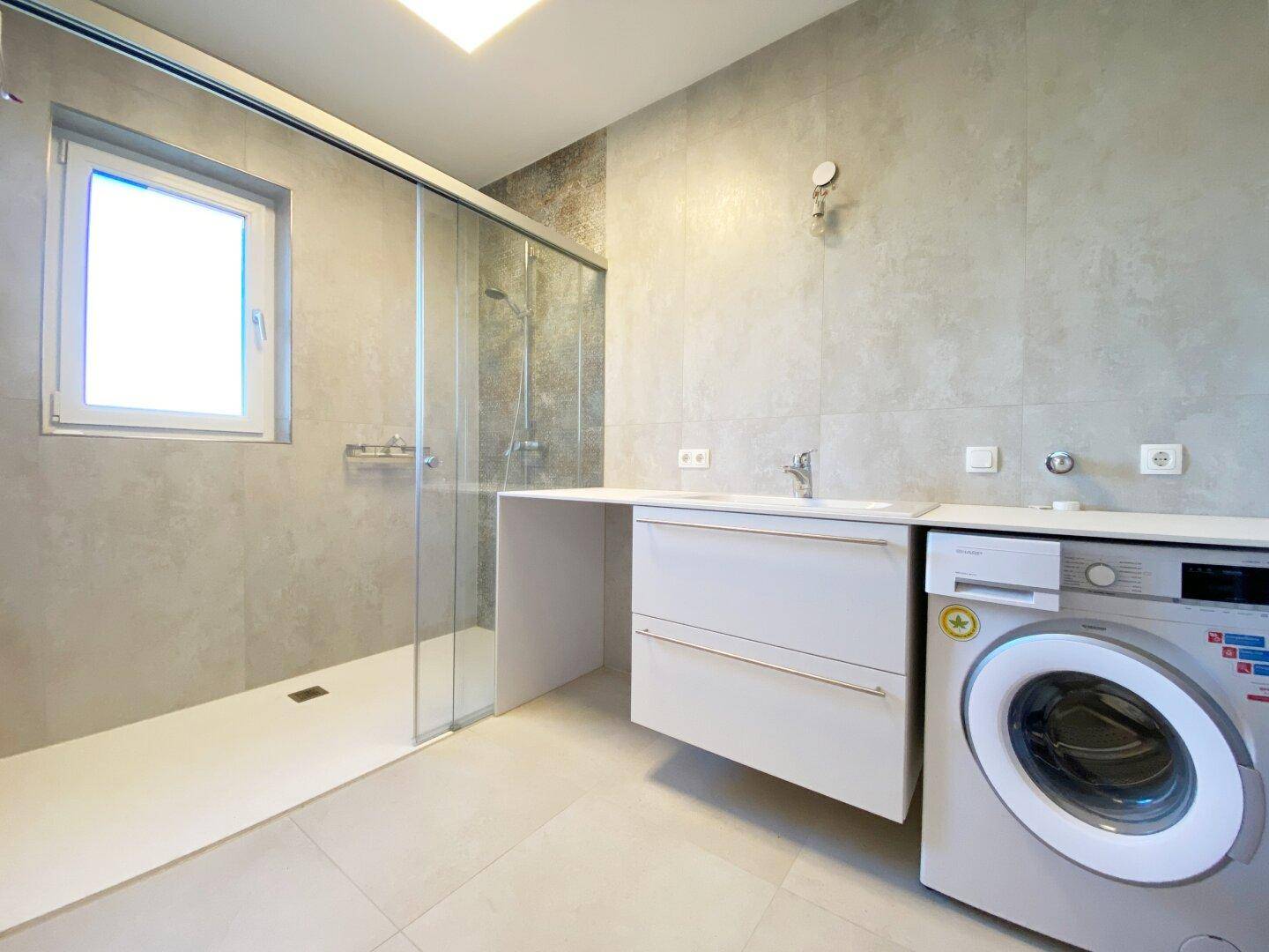 Modernes Badezimmer mit ebenerdiger Dusche, Waschbecken und integrierter Waschmaschine.