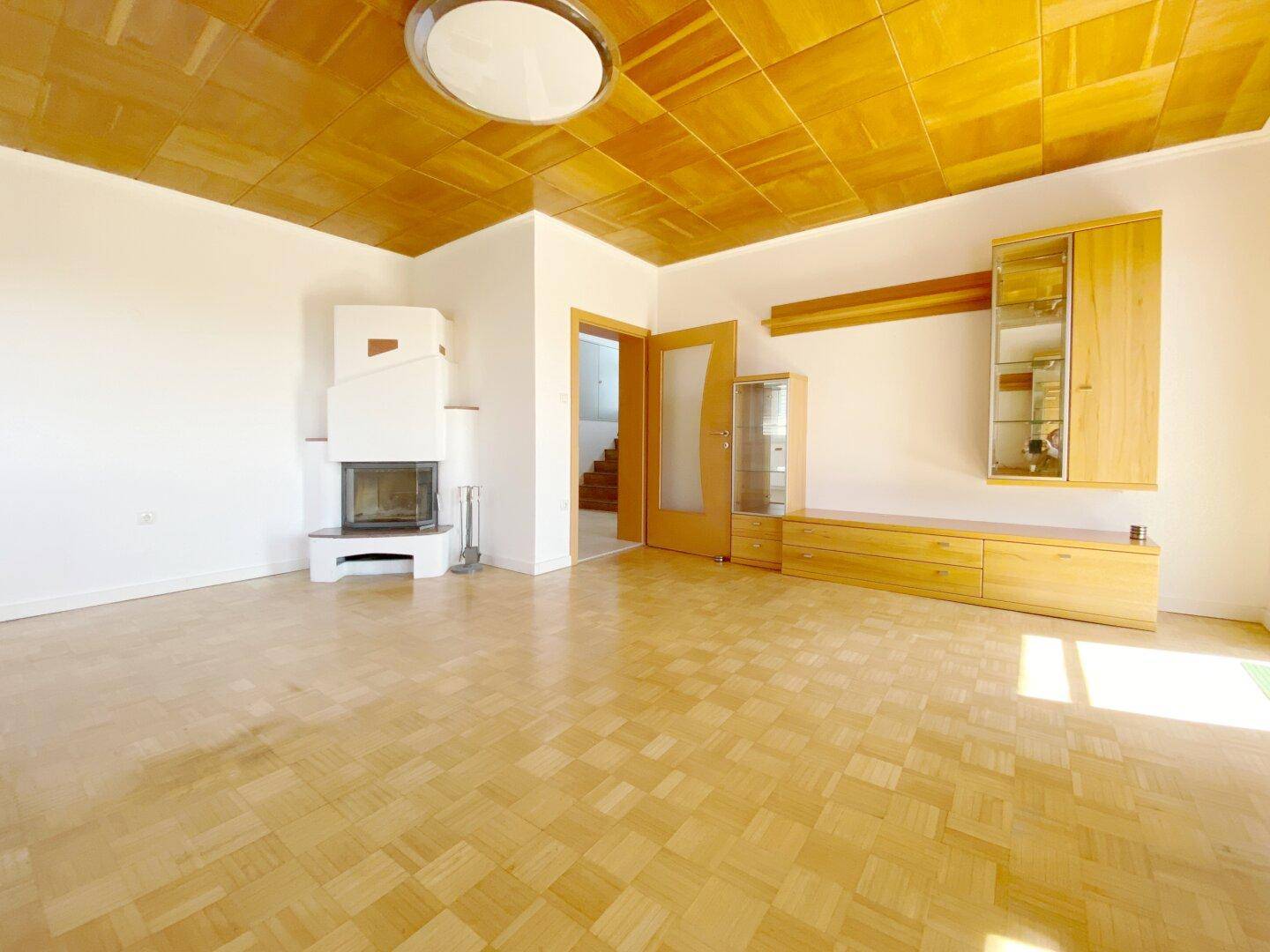 Geräumiges Wohnzimmer mit Parkettboden, Kamin und einer markanten Holzdecke.