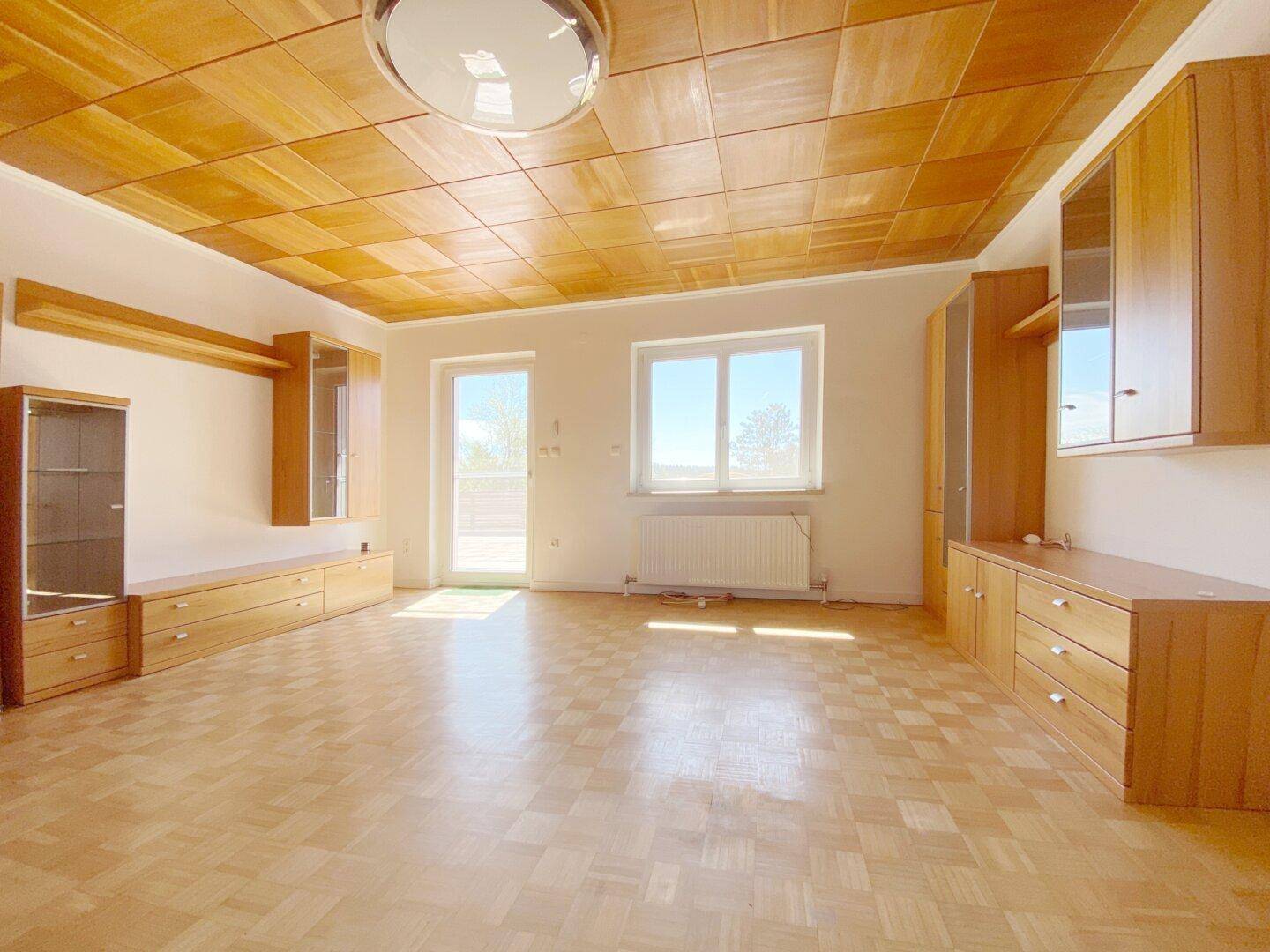 Helles Wohnzimmer mit Parkettboden, Holzdecke und Zugang zu einem Außenbereich.