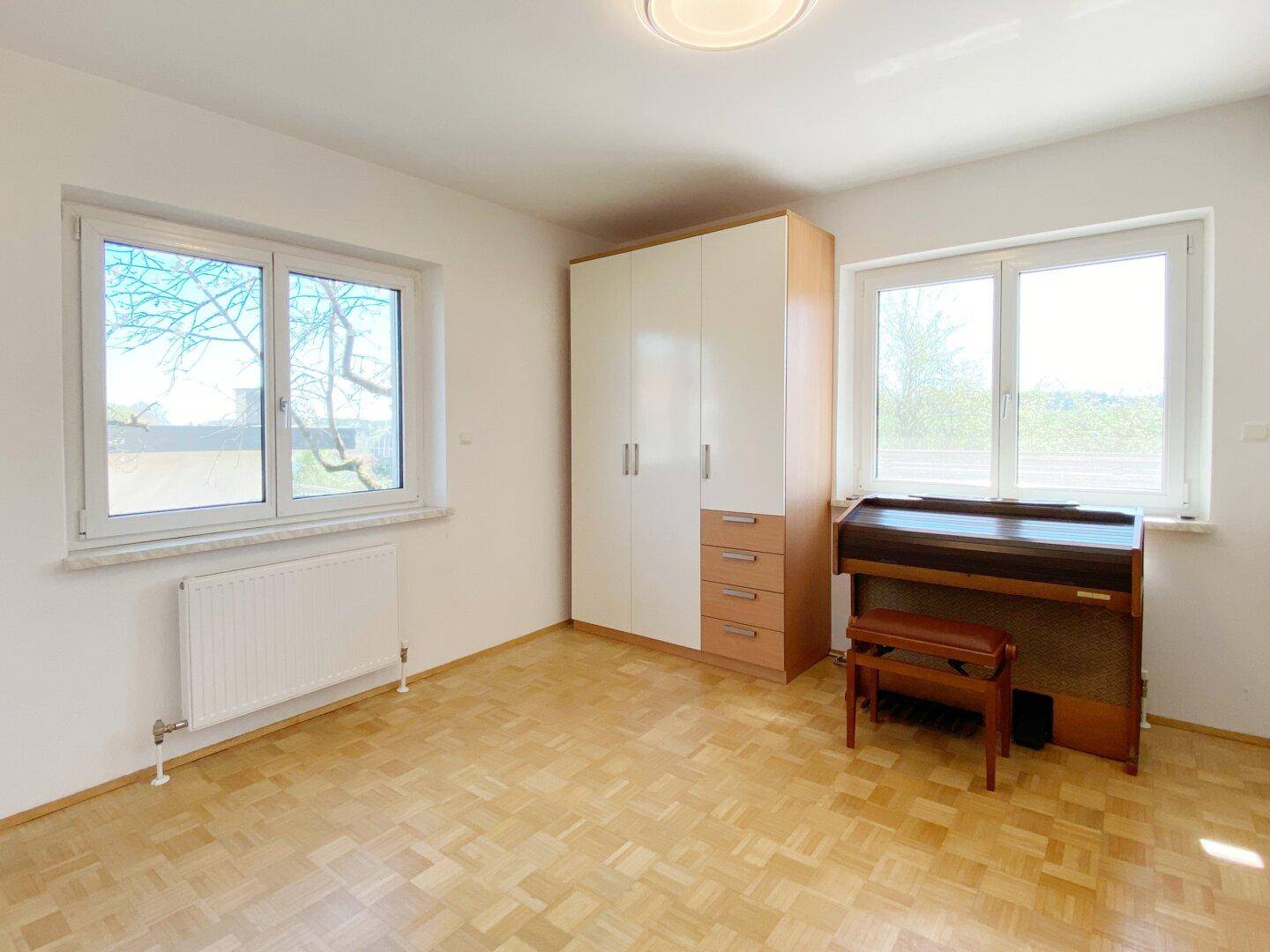 Helles Schlafzimmer mit Parkettboden, Kleiderschrank und zwei Fenstern für viel Tageslicht.