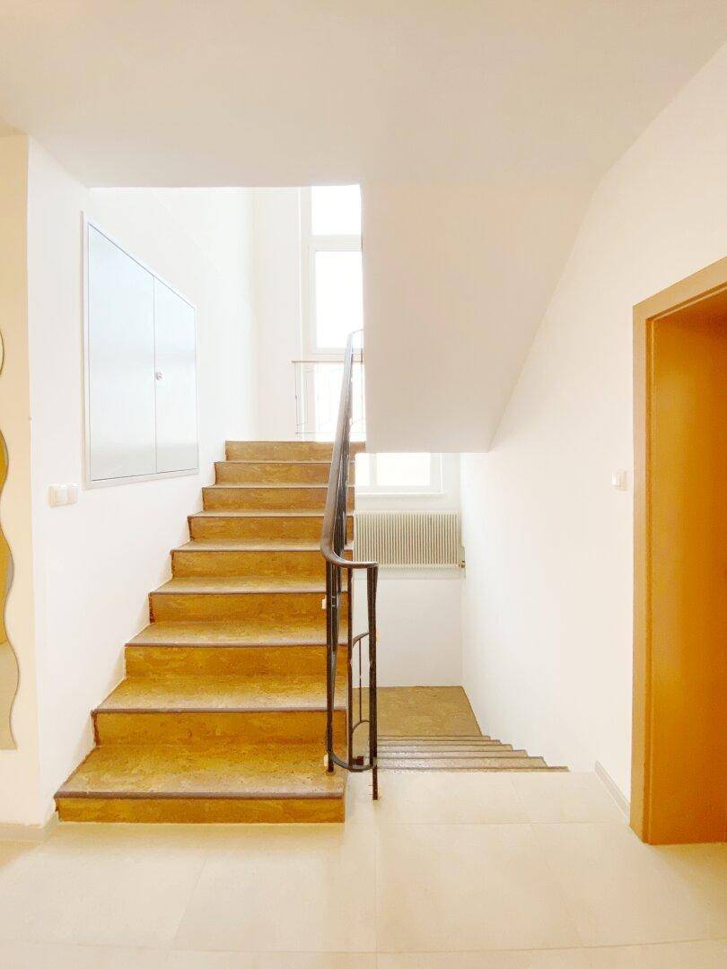 Helles Treppenhaus mit Holzstufen und einem schlichten Metallgeländer.