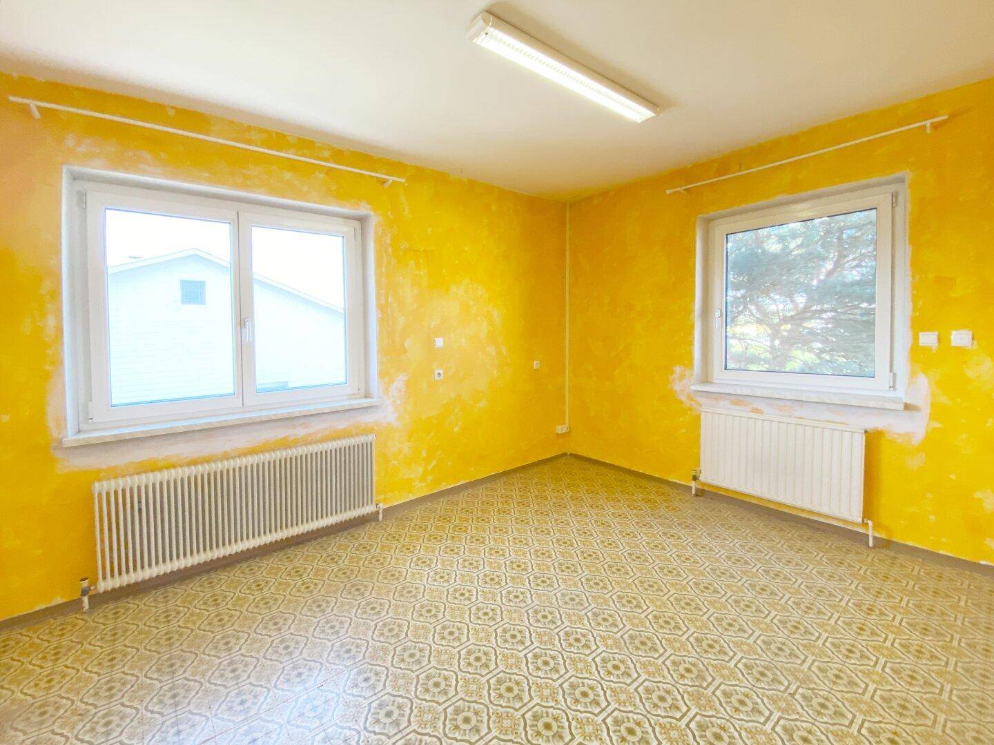 Raum mit gelber Tapete und gemustertem Bodenbelag, der Renovierungsbedarf aufweist.