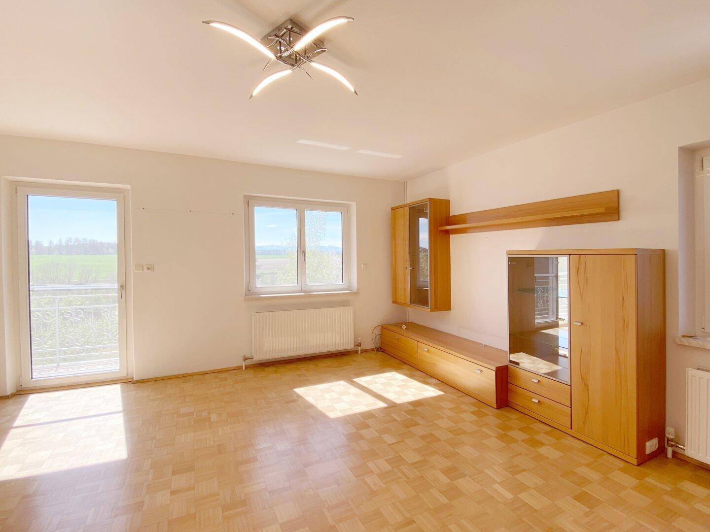 Helles Wohnzimmer mit Parkettboden und Zugang zu einem Balkon, der viel Licht hereinlässt.