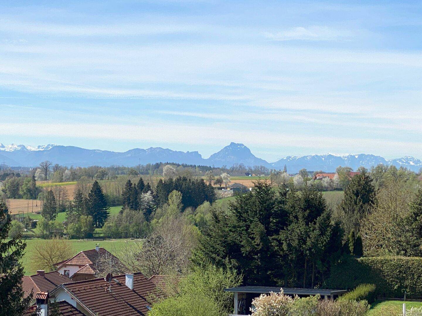 Weitläufiger Panoramablick über grüne Felder, Wälder und eine beeindruckende Bergkette am Horizont.