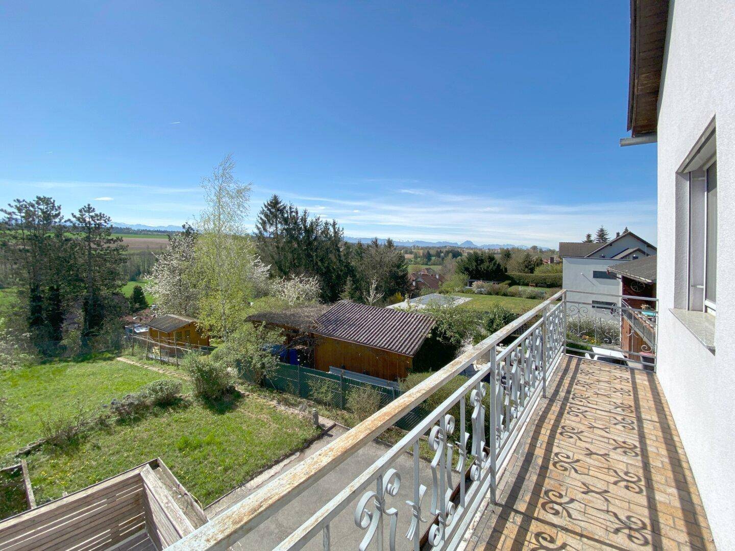 Balkon mit Metallgeländer und weitem Blick über die grüne Umgebung und entfernte Berge.