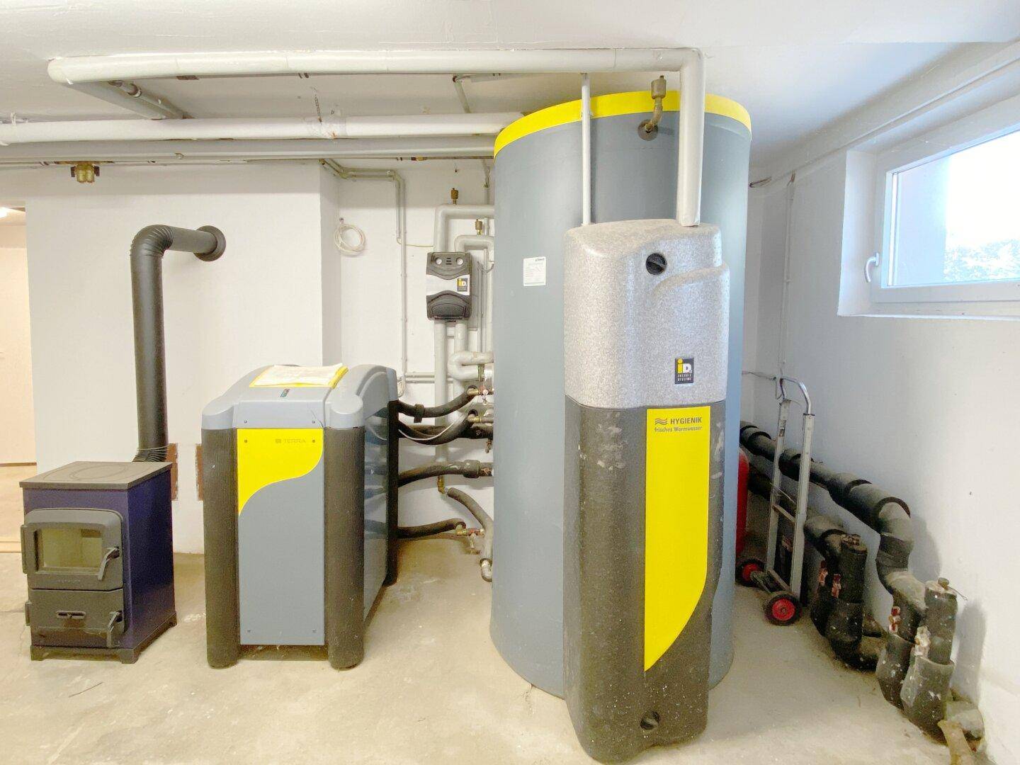 Heizraum im Keller mit moderner Wärmepumpe, Warmwasserspeicher und Holzofen.