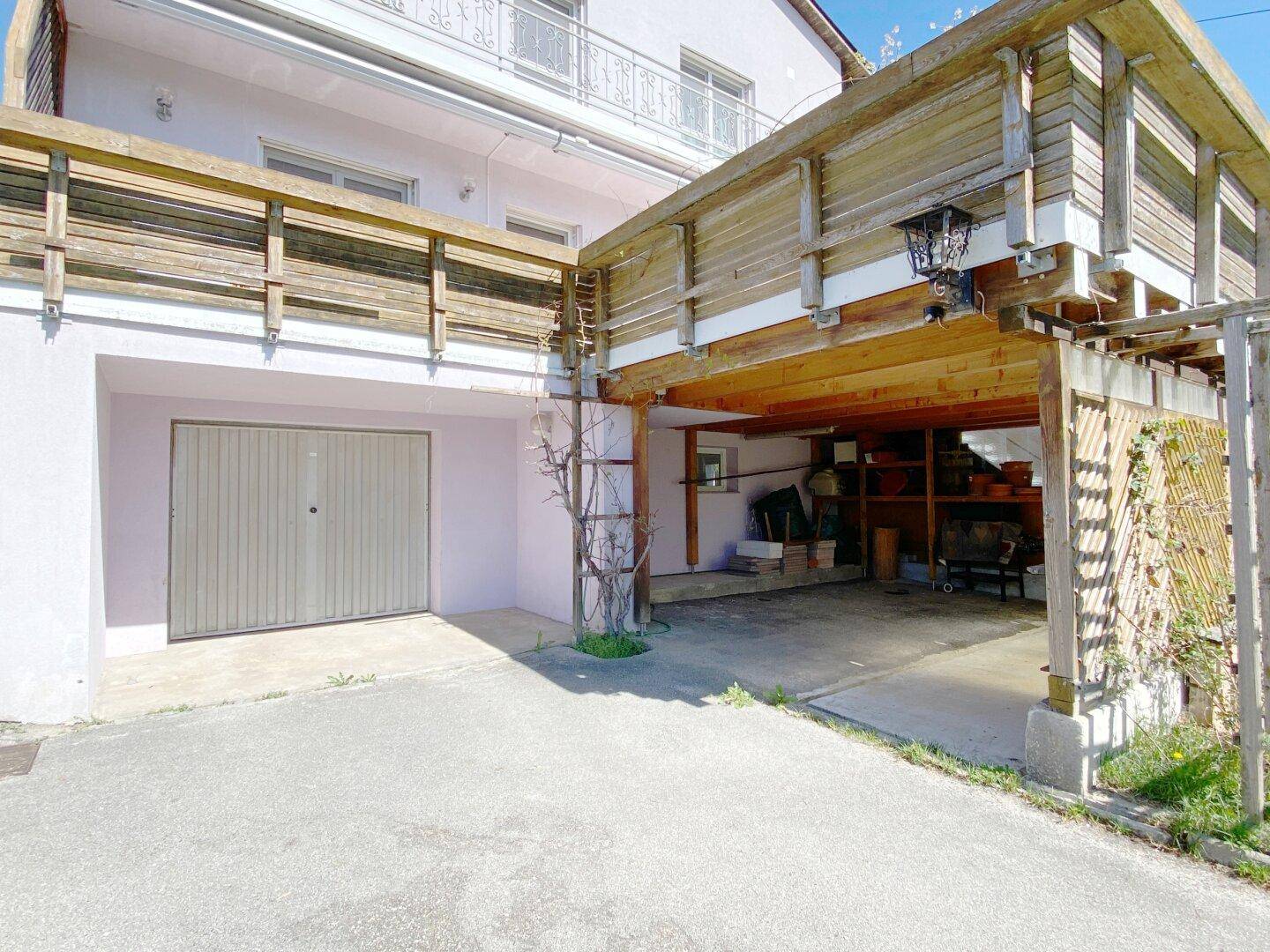 Hausfassade mit integrierter Garage und einem überdachten Carport im Außenbereich.