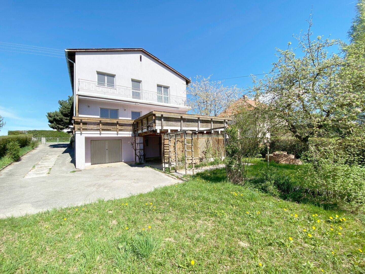 Rückseite des Hauses mit Garage, erhöhter Holzterrasse und Zugang zum Gartenbereich.