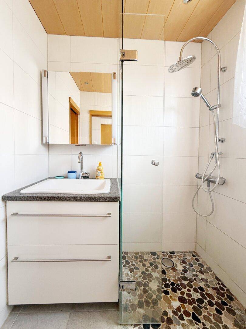 Helles Badezimmer mit moderner Dusche, Waschbecken und Spiegelschrank.