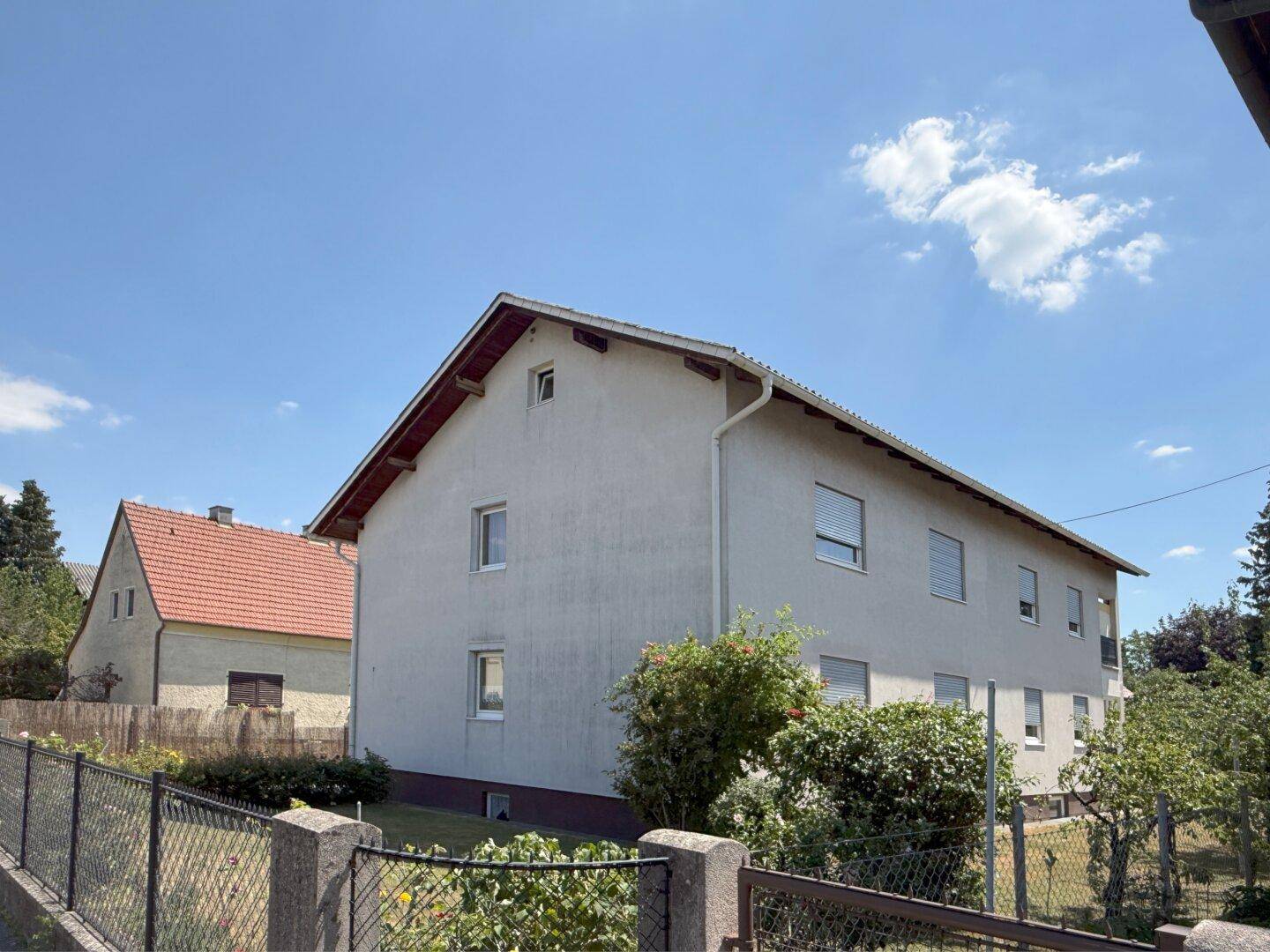Seitenansicht des Hauses mit schlichter Fassade und Fenstern unter blauem Himmel.