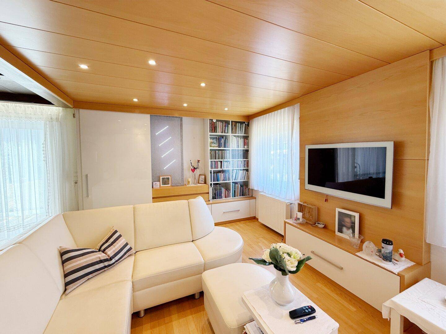 Geräumiges Wohnzimmer mit bequemer Eckcouch, Bücherregal und Holzdecke.