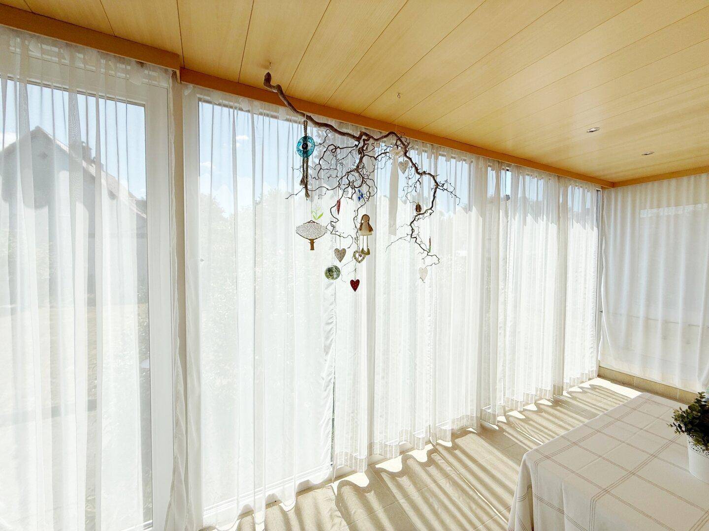 Lichtdurchfluteter Wintergarten mit raumhohen Fenstern und dekorativer Holzdecke.
