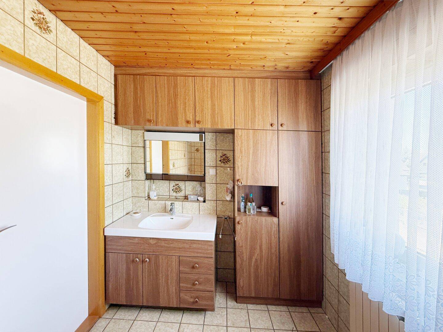 Badezimmer mit Waschbecken, Spiegelschrank und Holzschränken unter einer Holzdecke.