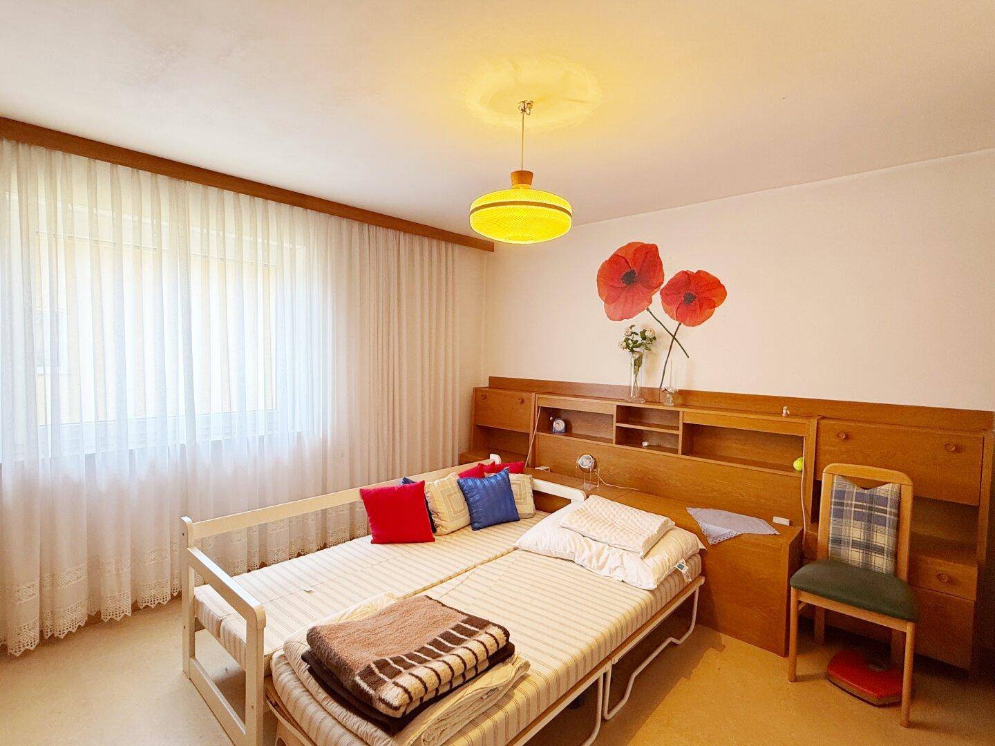 Helles Schlafzimmer mit zwei Einzelbetten, Holzmöbeln und dekorativen Wandbildern.